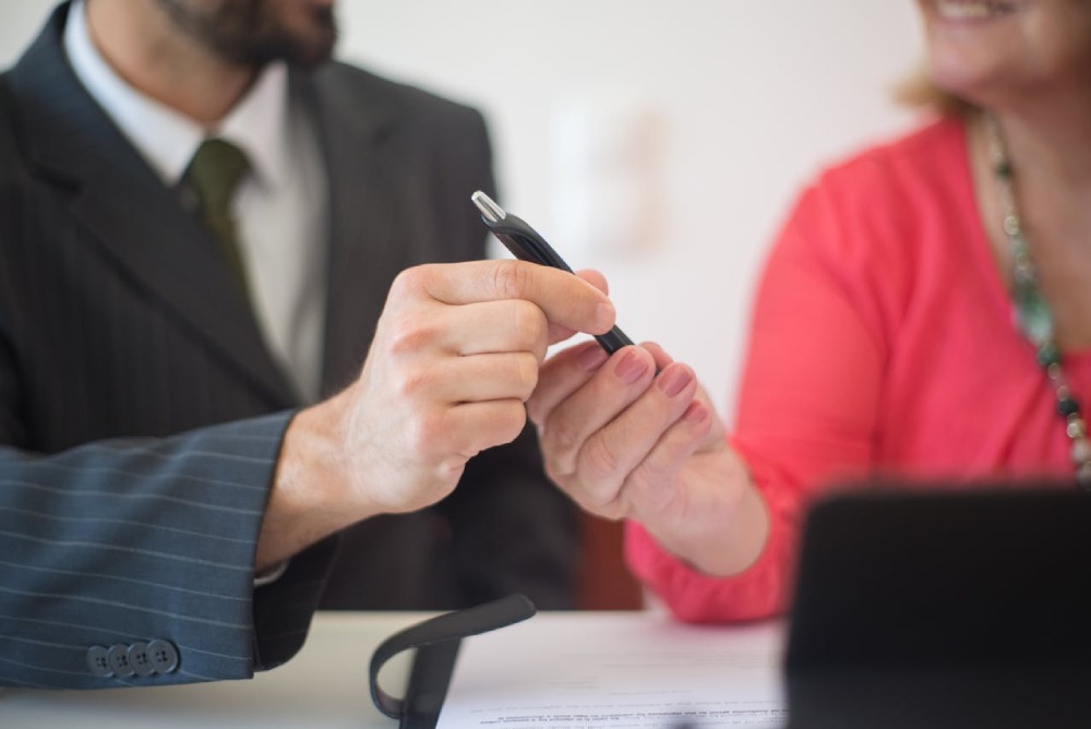 a person handing another a pen and signing paperwork